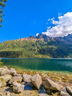 Pristine alpine lake with turquoise water white rocks and dense forest beneath Tatra mountain peaks near Zakopane Poland. High quality photograph