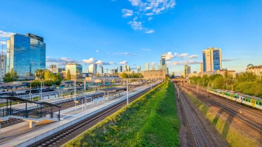 Varşova, Polonya, 20 Eylül 2025. Demiryolu altyapısı ve parlak mavi gökyüzü altında yeşil bitki örtüsünün yanında yüksek binaları olan modern şehir silueti. Yüksek kalite fotoğraf.