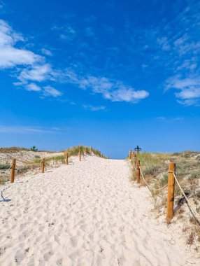 Sandy path with wooden fence leading through white dunes under blue sky near Leba Poland Baltic coast. High quality photograph