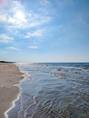 Gentle Baltic Sea waves rolling onto sandy beach shore under blue sky near Leba Poland coastline. High quality photograph