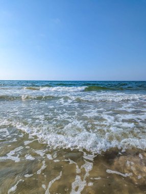 Foamy Baltic Sea waves washing sandy beach shore with green water under blue sky near Leba Poland. High quality photograph