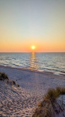 Leba Polonya yakınlarındaki Baltık Denizi sahilindeki çimlerin üzerinden gün batımı manzarası turuncu güneş suyu yansıtıyor. Yüksek kalite fotoğraf