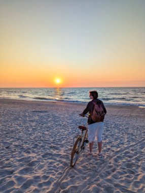 Altın saat boyunca Leba Polonya yakınlarındaki Baltık Denizi sahillerinde bisiklet süren kişi gün batımını seyrediyor. Yüksek kalite fotoğraf