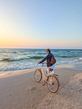 Baltık Denizi sahilinde bisiklet süren bayan bisikletçi Leba Polonya yakınlarında altın gün batımında kıyı manzarasının tadını çıkarıyor. Yüksek kalite fotoğraf