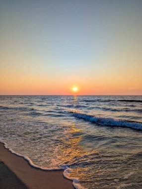 Baltık Denizi dalgalarını aydınlatan ılık gün batımı ışığı ve Leba Polonya yakınlarındaki kumlu plaj sakin kıyı atmosferi yaratıyor. Yüksek kalite fotoğraf