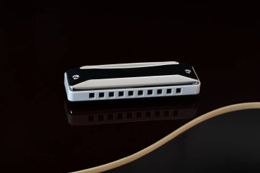 Makro akustik gitar gövdesinin arkasında yatan diyatonik mızıkayı kapat ve gitar gövdesinin yansımasını ve eğrisini göster