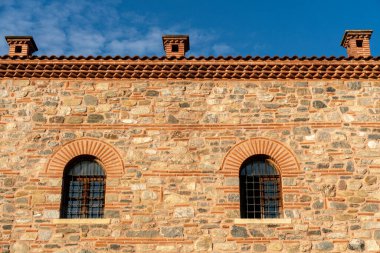 Açık mavi gökyüzüne karşı bacaları ve pencereleri olan canlı bir bina duvarı.