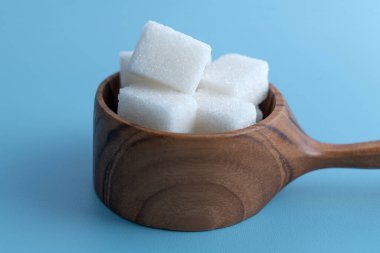 Tahta bir ölçü kabının üzerinde mavi bir zemin üzerinde duran şeker küplerinin ön görüntüsü