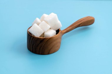 Ahşap bir ölçü kabındaki şeker küplerinin mavi bir zemin üzerindeki ön görünümü; günlük tüketim şekerini ölçün