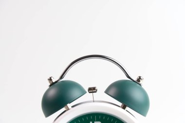 Beyaz alarm saatinin ikiz zilli ve saat tuşlu ön plan fotoğrafı koyu yeşil ve alarm beyaz zemin üzerinde saat 4 'ü 30 geçe ayarlanmış.