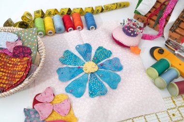 Kumaş dikme, dikiş dikme, iğne işi. Çiçek dikmeye hazır uygulama, bükülmüş sarı bir mezura, yorgan ipliklerinin çok renkli makaraları, ve beyaz arkaplana yerleştirilmiş iğneli iğne.