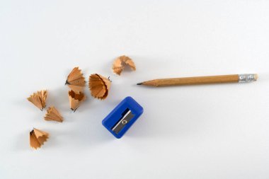 Bir kalem, kalem talaşı ve beyaz bir arkaplanda zarif bir şekilde düzenlenmiş mavi bir bileyici. Basit ve klasik kırtasiye malzemelerini sergiliyor.