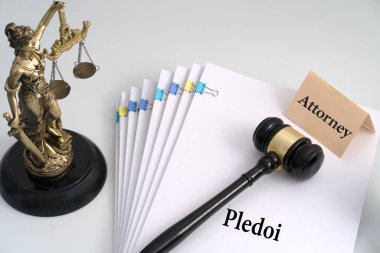 'Pledoi' başlıklı bir yığın belgenin yanında duran bir heykel, üzerinde 'Avukat' yazan bir tokmak, yasal savunmayı, savunmayı ve adaletin yerini bulmasını simgeliyor.