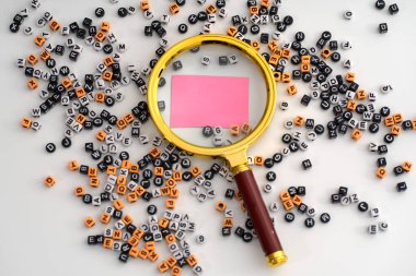 Bir büyüteç altında büyütülmüş, keşfedilme, yorumlama ve anlamın oluşumunu sembolize eden, dağınık harf ve sayı çeşitleriyle çevrili, boş bir pembe kağıt parçası.