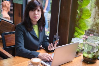 kafede dizüstü bilgisayar ve akıllı telefon kullanan kadın