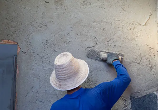 Duvarı alçılayan uzun malalı inşaat işçisi.