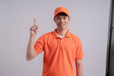 Turuncu gömlekli gülümseyen adamın portresi gri arka planda baş parmak hareketi gösteriyor.