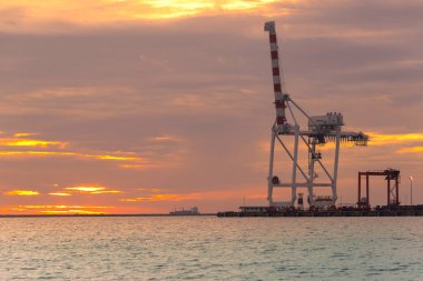 Gün batımında kargo vinci ve konteyner gemisinin silueti.