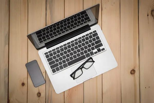 Laptop, akıllı telefon, defter ve kalemle modern ahşap ofis masasının üst görüntüsü. Kopyalama alanı mevcut.