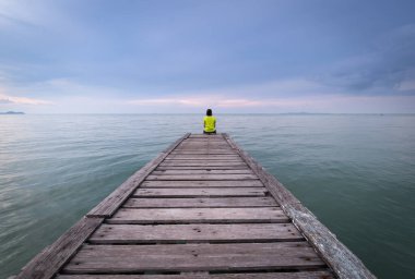 Denizin tahta köprüsünde tek başına oturan bir kız. Yalnız oturan bir kadın Vintage tarzı.