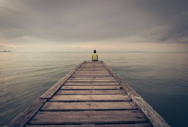 Denizin tahta köprüsünde tek başına oturan bir kız. Yalnız oturan bir kadın Vintage tarzı.