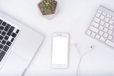 Akıllı telefonlu modern beyaz ofis çalışma masası dizüstü bilgisayarı, kulaklığı ve kedisi, üst görünümü.