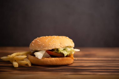 Peynirli hamburger ve ahşap masada kızarmış patates.