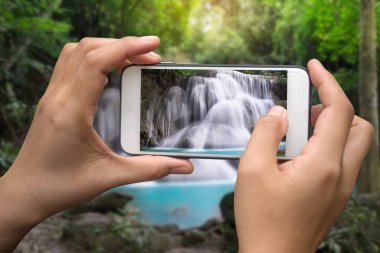 Turist çekim bir fotoğraf şelale içinde smartphone ile derin orman.