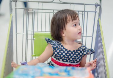 Alışveriş sepeti ile küçük kız. Alışveriş Sepeti Alışveriş Merkezi yakınında oturan çocuk. Mutlu gülümseyen çocuk arabası arabasında oturuyor. Satış ve alışveriş