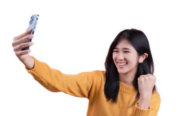 Bir kadın cep telefonuyla selfie çekiyor, gülümsüyor ve elini havaya kaldırıyor.