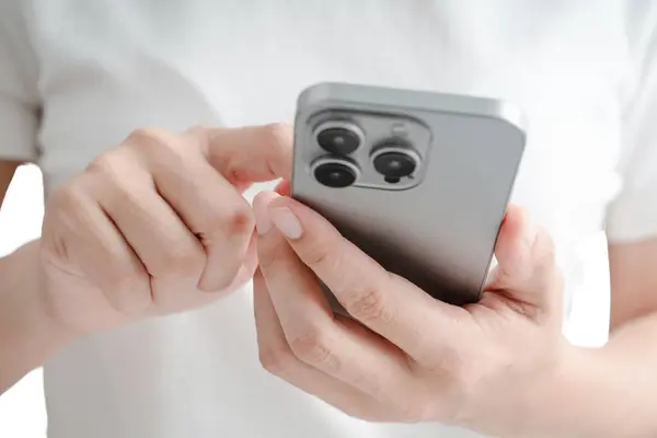 Bir kadın cep telefonunu tutuyor ve ona bakıyor. Telefondaki bir düğmeye basmak için baş parmağını kullanıyor.