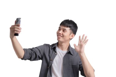 Genç bir adam cep telefonuyla selfie çekiyor, gülümsüyor ve kameraya el sallıyor. Mutluluk ve dostluk kavramı, bu anın tadını çıkarıyor ve bunu başkalarıyla paylaşıyor.