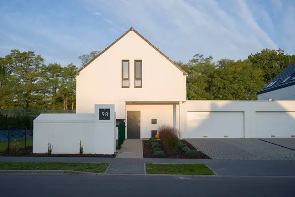 Minimalist beyaz cepheli ve birbirine bağlı garajı olan modern bir tek aile evi. Mülk güneşli bir günde sakin bir banliyö mahallesinde yer alır. Ön bahçe çalılarla döşenmiş ve giriş bir WR ile dekore edilmiş.