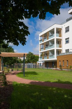 Güzel peyzajlı iç avlusu olan modern bir apartman dairesi. Bahçede yemyeşil bir çimen, bir yürüyüş yolu ve sakinlerin dinlenmesi için bankları olan ahşap bir pergola bulunuyor. Binanın çağdaş bir tasarımı var.