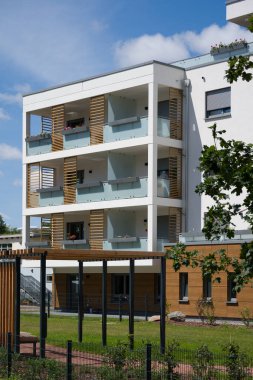 Peyzajlı iç avlusu olan modern bir apartman dairesi. Bina, beyaz bir cephe, ahşap panelli aksanlar ve cam parmaklıklar ve dekoratif ahşap kaplamalarla birçok şık balkonlara sahip çağdaş bir tasarıma sahip.