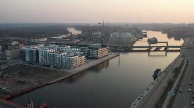 Polonya 'nın Szczecin kentinin hava perspektifi, Odra Nehri boyunca çağdaş kentsel gelişimi sergiliyor. Ön planda, geniş bir yol ve nehir kenarındaki gezinti alanı suya paraleldir. Manzara, yeni ve çağdaş bir konut kompleksini vurguluyor,
