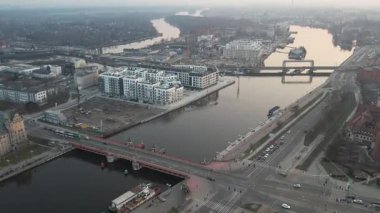 Polonya, Szczecin 'in panoramik hava manzarası, gün batımında. Görüntü, köprüden ve rıhtım boyunca ilerleyen trafik ile hareketli şehir yaşamını yakalıyor. Yeni mimari gibi modern mimarinin dinamik karışımını sergiliyor.