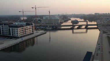 Aerial view of the Szczecin city center in Poland during a scenic sunset. Oder river with new, modern apartment buildings on the Lasztownia island. In the background, construction cranes are visible, symbolizing the urban development.