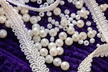 Dağıtılmış beyaz inciler ve zarif bir kurdele desenli mor kumaşın üzerinde. Düşük bir açıyla çekilen kompozisyon, sakin bir atmosferi taşır..