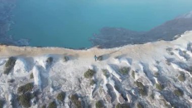 Erkek dağcının turkuaz sülfür gölü ve sülfür dumanı manzaralı aktif volkana tırmanması.