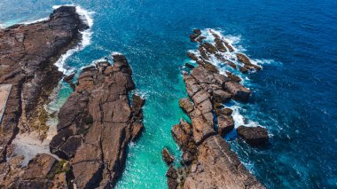 Dramatik okyanus dalgaları kayalık kıyılara çarpıyor, turkuaz su gün ışığında parıldıyor.