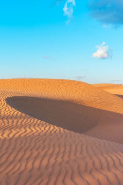 Mavi gökyüzünün altında kumlu turuncu bir kum tepesi