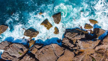 Atlantik okyanus dalgalarının drone görüntüsü su altındaki kayalıklarla birleşiyor. Büyük dalgalı mavi dalgalar kayalara çarpıyor.