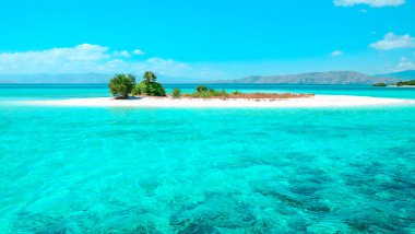 Beyaz kumlu güzel tropik plaj, turkuaz okyanus, güneşli yaz gününde bulutlu mavi gökyüzüne karşı.