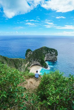Uçurumun önünde oturan ve Kelingking Sahili 'nde denize bakan adam, Nusa Penida, Endonezya.