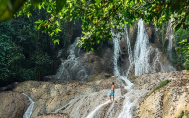 Kayanın üzerinde duran adam güzel şelale manzarasının tadını çıkarıyor.