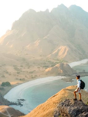 Sırt çantası ve sırt çantalı genç bir gezgin gün doğumunda dağ yolunda yürüyor..