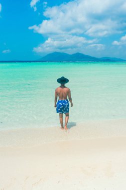 Genç adam tropikal sahilde durup denize bakarak eğleniyor ve rahatlıyor. Yaz tatili ve yaz tatili konsepti.