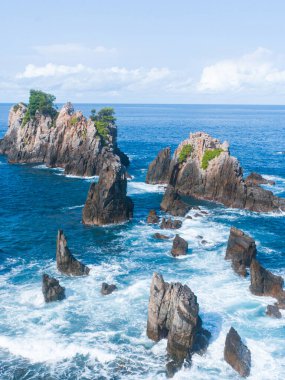 Okyanusun kayalık kıyıları, kayalar, dalgalar, mavi sular.