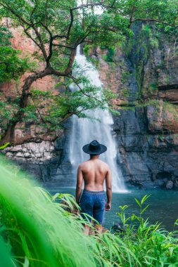 Genç bir adam ormanda şelalenin tadını çıkarıyor.
